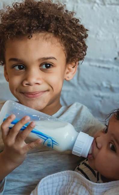 A young boy smiling while feeding his baby sibling